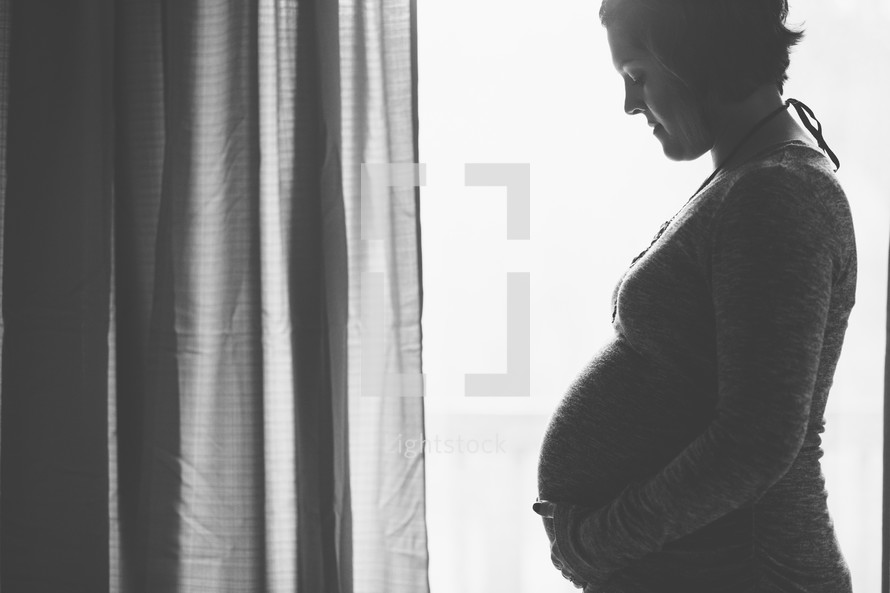 pregnant woman standing in front of a window 
