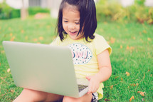 a little girl sitting in the grass with a laptop on her lap 
