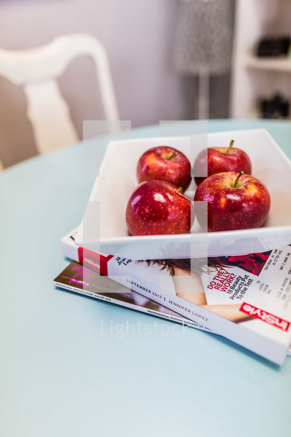 Bowl of red apples on table with magazines