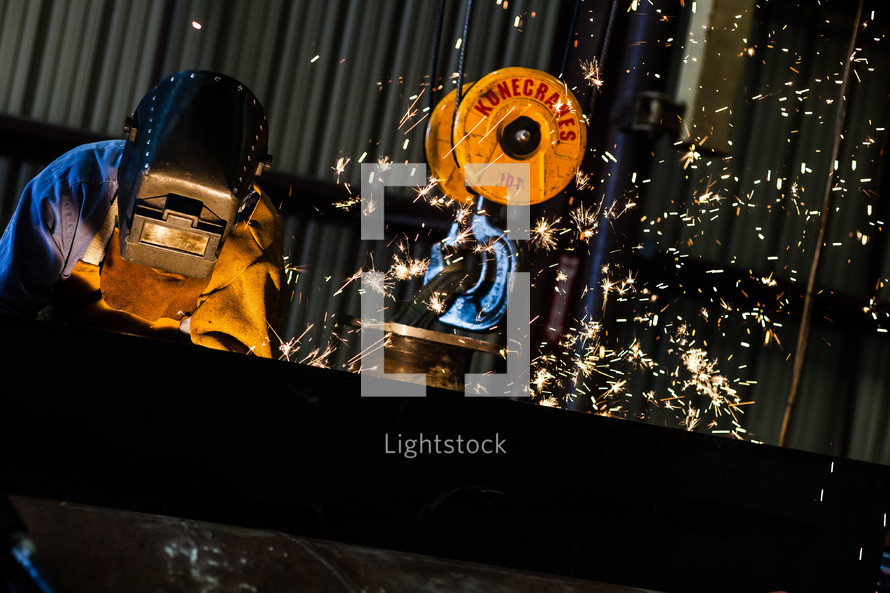 Sparks flying as Man welding welder hood mask industrial steel crane air arcing 