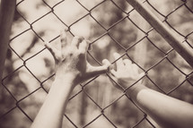 grasping hands on a chain link fence 