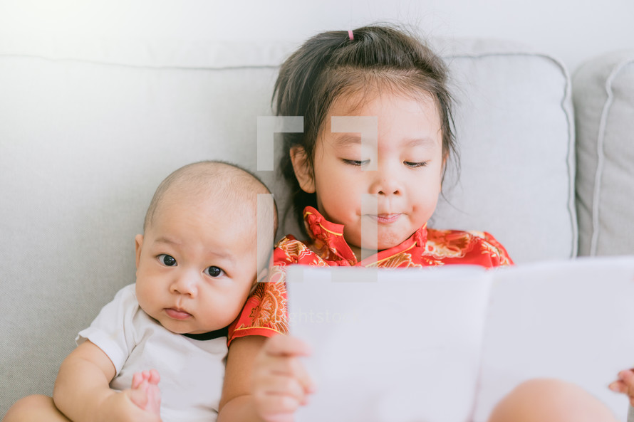 big sister reading to her infant brother 