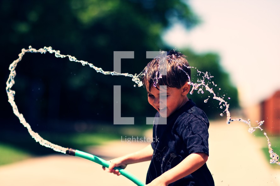 A young boy playing with a water hose 