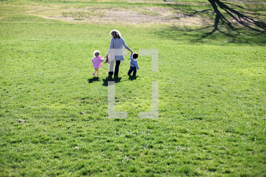 A mother holding hands and walking with her children in a field of grass.