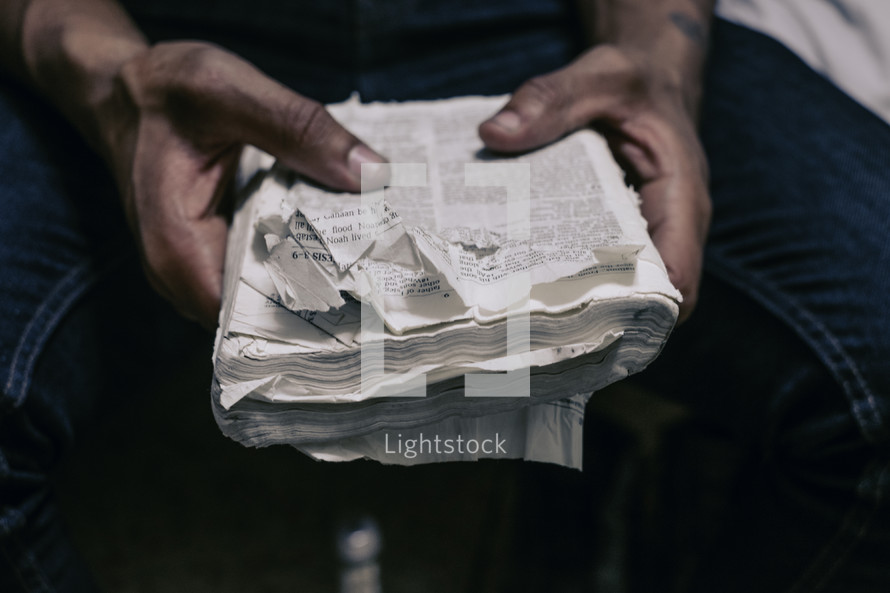 hands of a man holding an old worn and torn Bible 