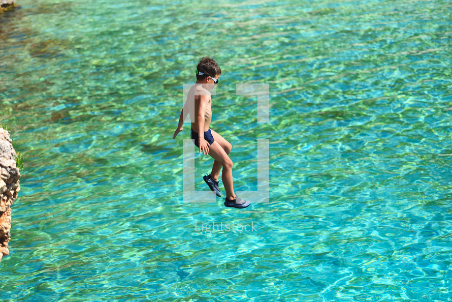 Little boy jumping off cliff into the ocean. Summer fun lifestyle. Brave kid