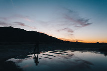 man standing at a lake shore at sunset 
