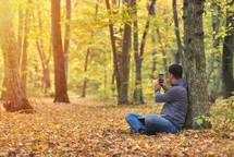 Man taking pictures with smartphone in forest, autumn colors