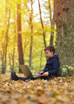 boy with laptop in forest, autumn colors, sunset warm light
