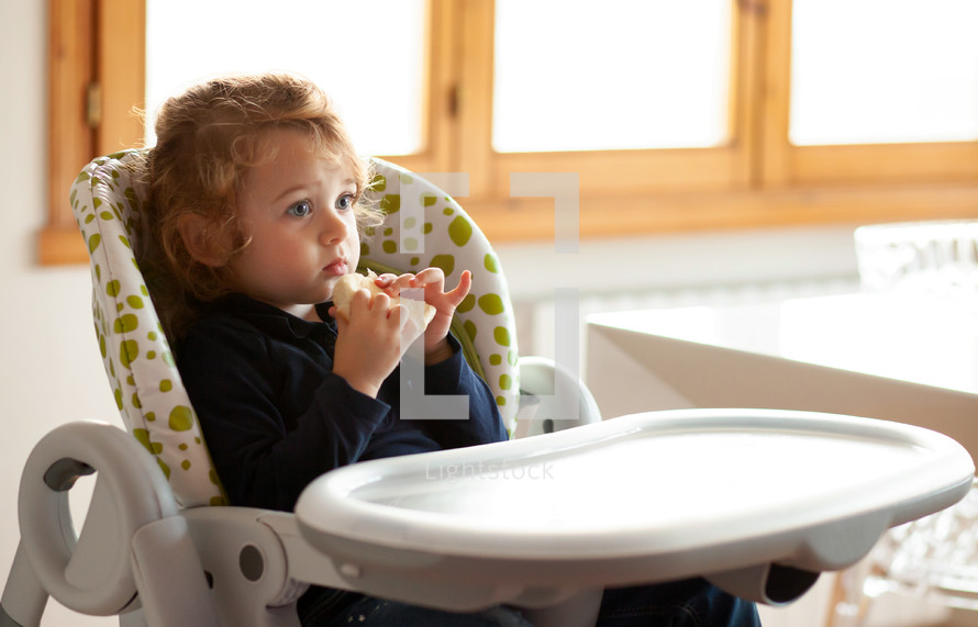 child eating bread in a highchair 