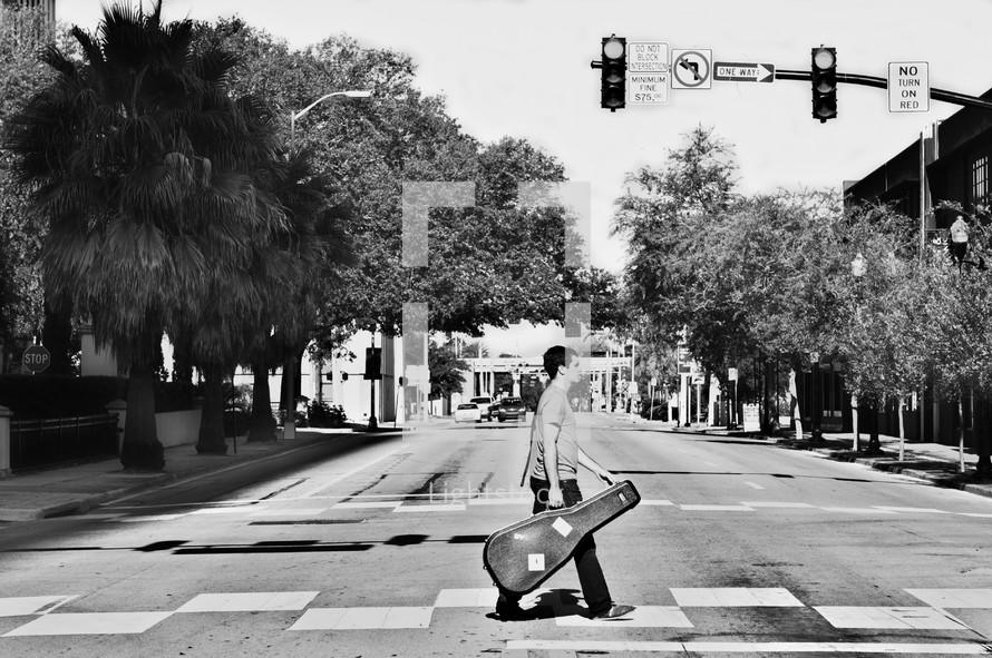 A man with a guitar crossing an intersection.