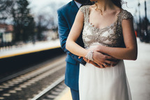 bride and groom standing by train tracks 