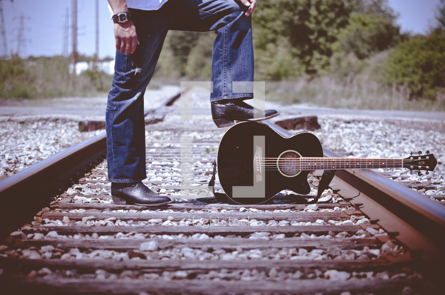 man standing on train tracks with his guitar 