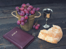 breaking the bread, with wine, grapes and Bible in the background
