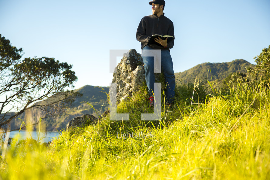 man sitting on a rock reading a Bible 