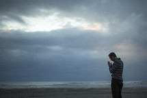 man standing with praying hands on a beach 