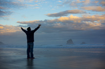 silhouette of a man with raised hands standing on a beach 