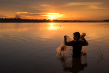 a man standing in a lake with a fishing net at sunset 