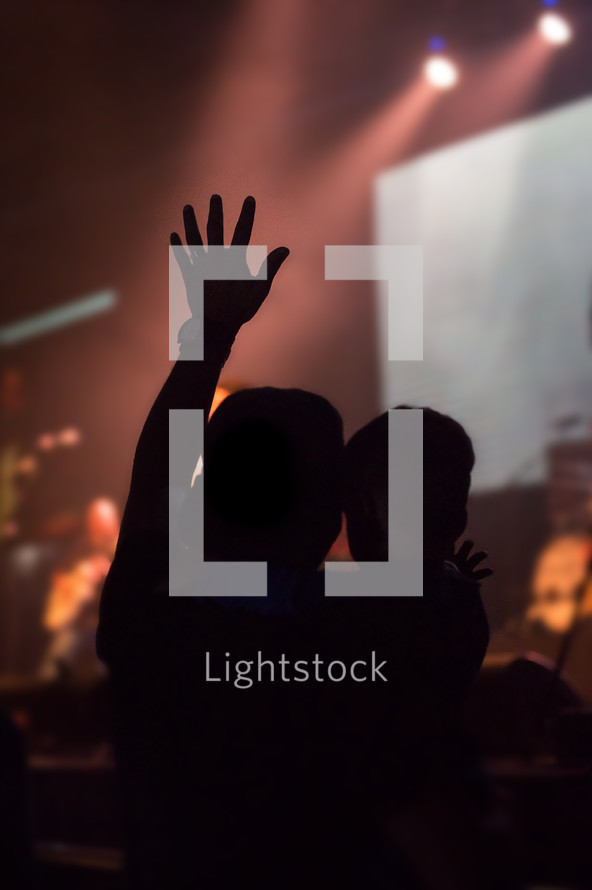 silhouette of a man holding a boy with a raised hand at a concert 