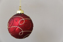Red and gold hanging Christmas ornament against white background