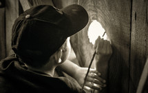 Boy looking through a hole in a barn door.