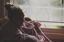 girl cuddled up in a blanket on a cold rainy day