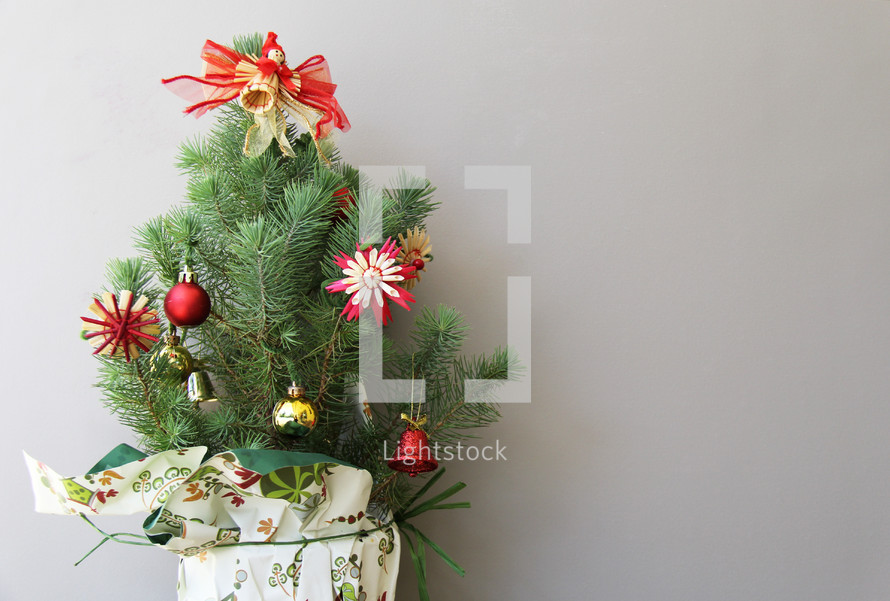 Small decorated Christmas tree with angel and presents against white / grey background