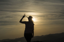 silhouette of a woman standing on a mountain top at sunset 