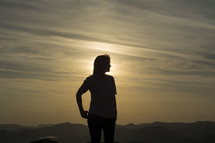 silhouette of a woman standing on a mountaintop at sunset 