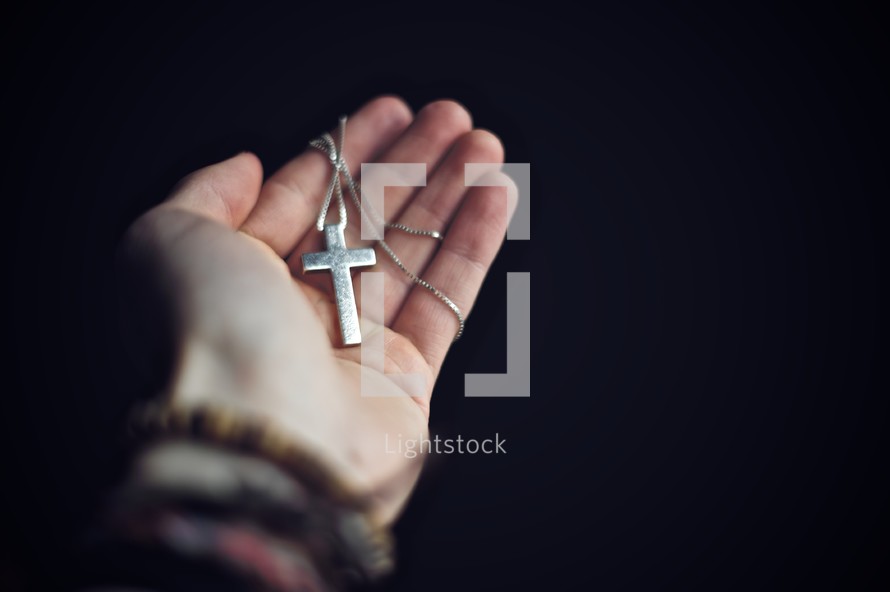 Hand holding a cross pendant and necklace.