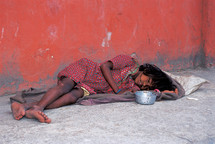 a homeless child sleeping on concrete with begging bowl