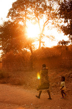 Mother and child walking down a dirt road in Malawi, Africa at sunset. 