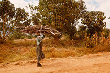 Man carrying a bundle of sticks along a dirt road.