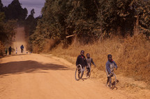 Children riding bicycles on a dirt road in Malawi Africa.