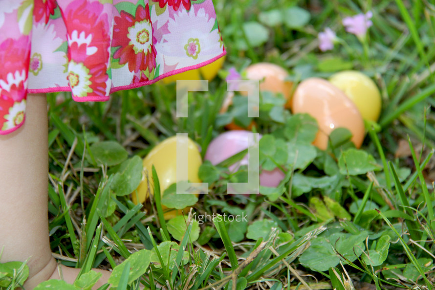 child's feet next to plastic Easter eggs in the grass