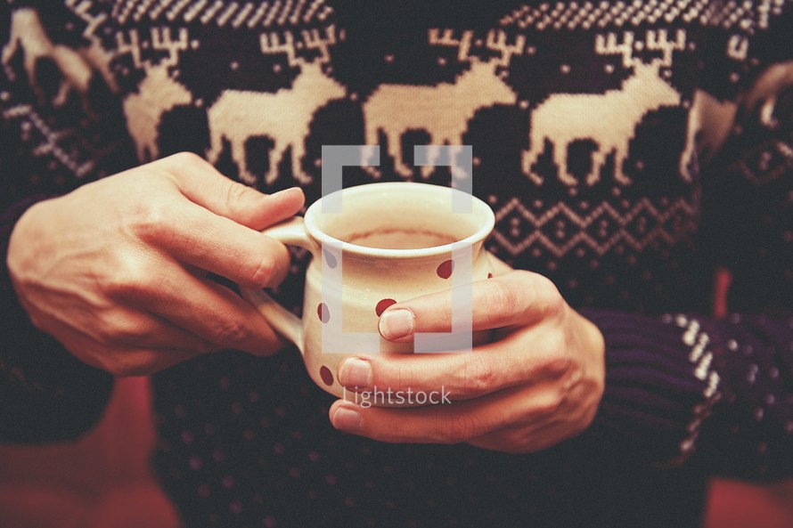 a man in a winter sweater holding hot chocolate 