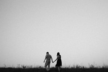 A man and woman walking through a field holding hands.