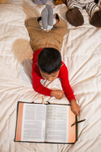 child reading a Bible in bed 