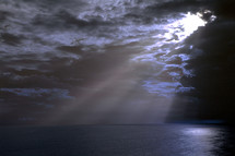 Dark storm clouds opening with rays of light radiating through over the Atlantic ocean