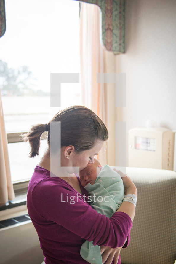 A woman holds a newborn baby in a hospital room.
