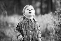 a toddler boy standing outdoors in a jacket looking up