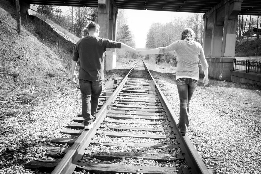 a couple holding hands walking on train tracks 