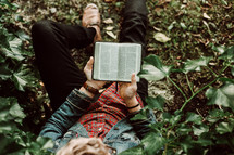 a young man sitting on the ground reading a Bible 