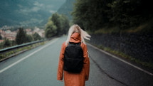 a woman in rain gear backpacking down a rural road 