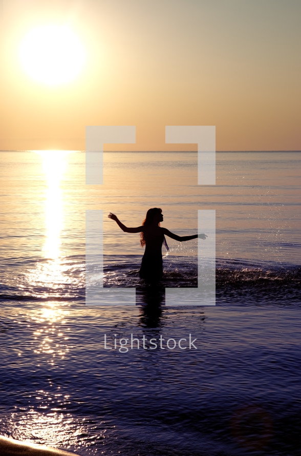 a young woman walking into water at sunset 