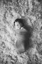 swaddled baby on a fur rug 