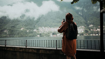 a woman in a rain coat taking a picture outdoors 