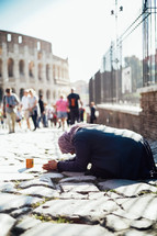 a beggar kneeling on cobblestone streets in Italy 