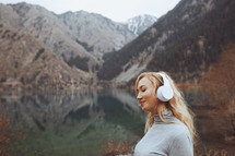 Woman wearing wireless headphones at the mountain lake