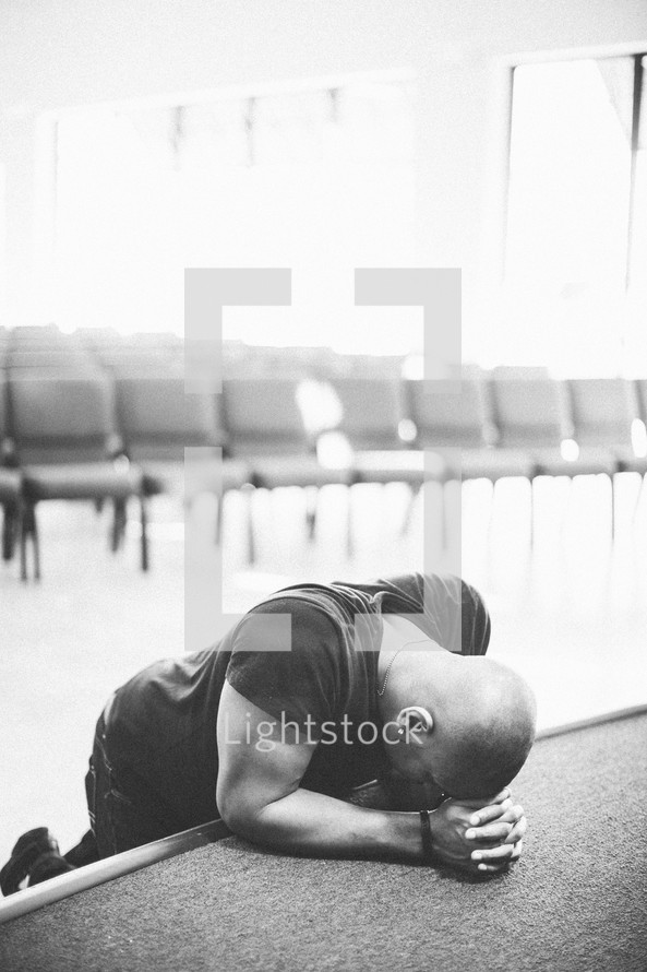 Man with head on hands praying on empty stage.